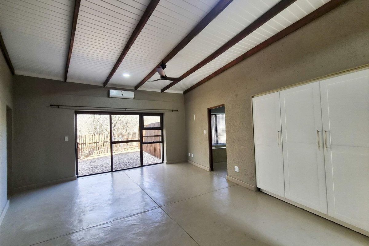 Spacious bedroom featuring polished concrete floors, exposed timber ceiling beams, built-in cupboards, and a sliding glass door leading to the exterior.