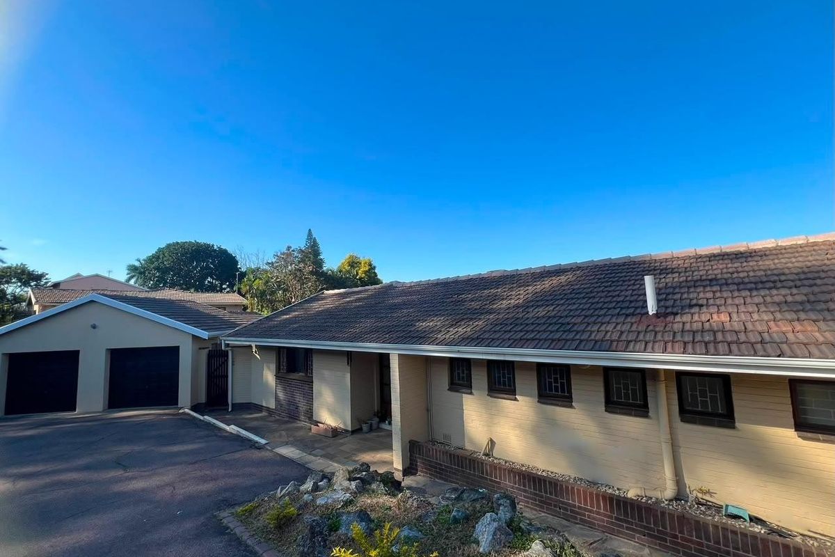 Front exterior view of a single-story brick house featuring a tiled roof, double garage, and paved driveway area.
