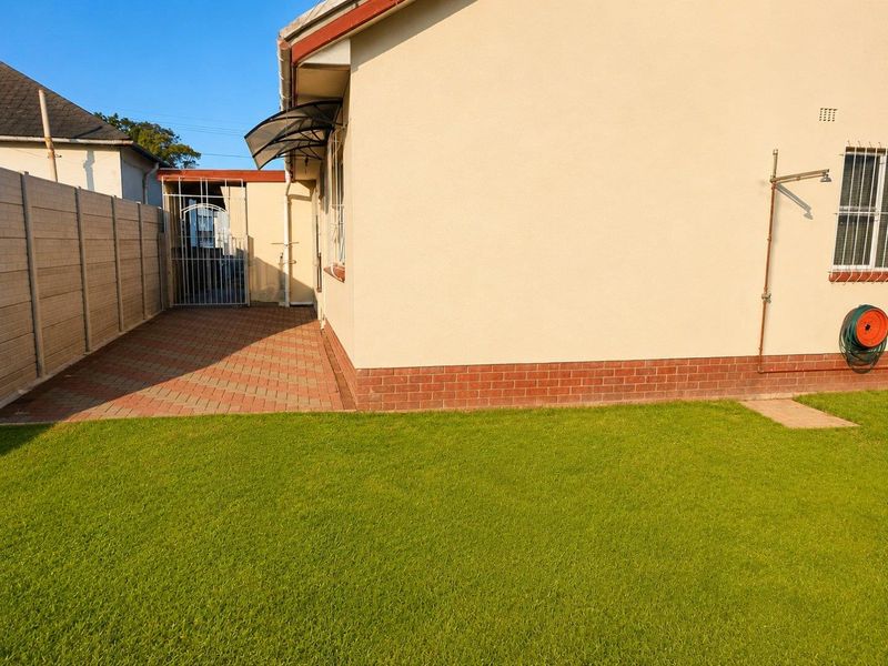 A well-maintained rear exterior view featuring a paved patio area, a neat lawn, and secure perimeter walling.