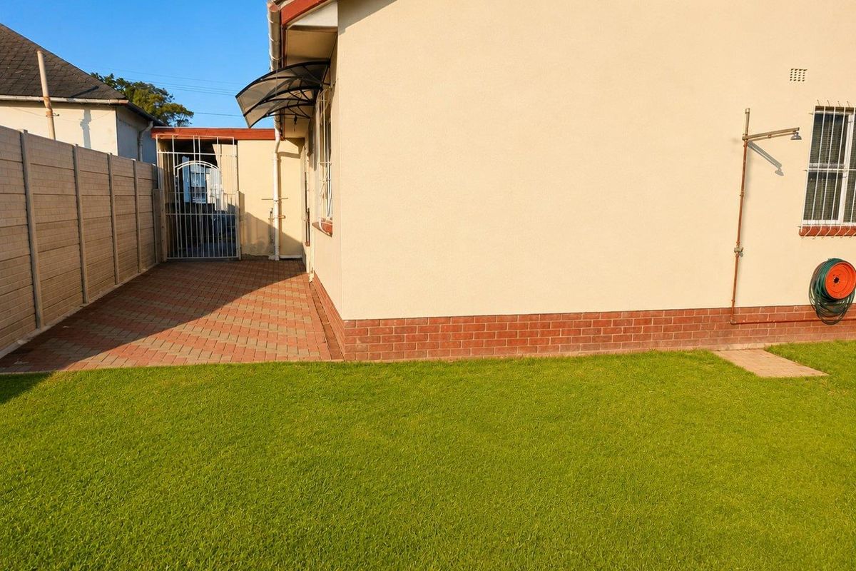 A well-maintained rear exterior view featuring a paved patio area, a neat lawn, and secure perimeter walling.