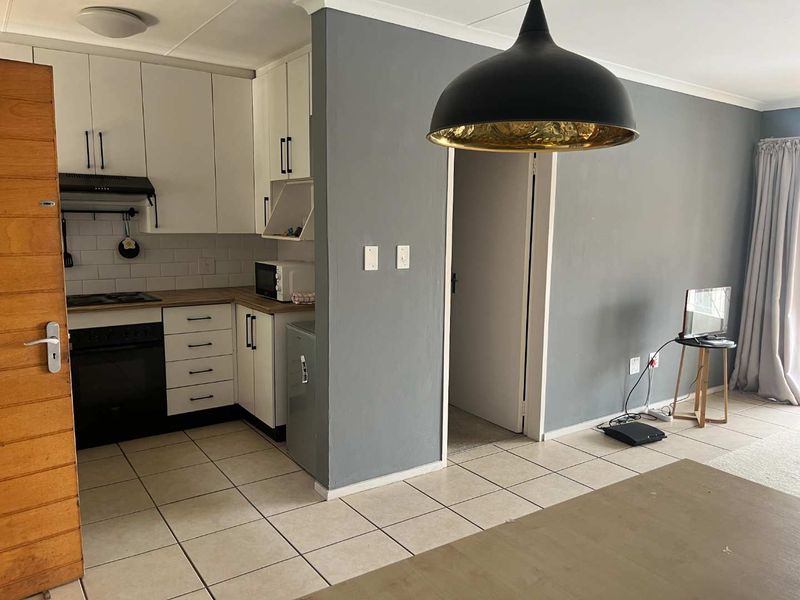 Open-plan kitchen and living area featuring white cabinetry, dark countertops, subway tile backsplash, and neutral tiled flooring throughout.