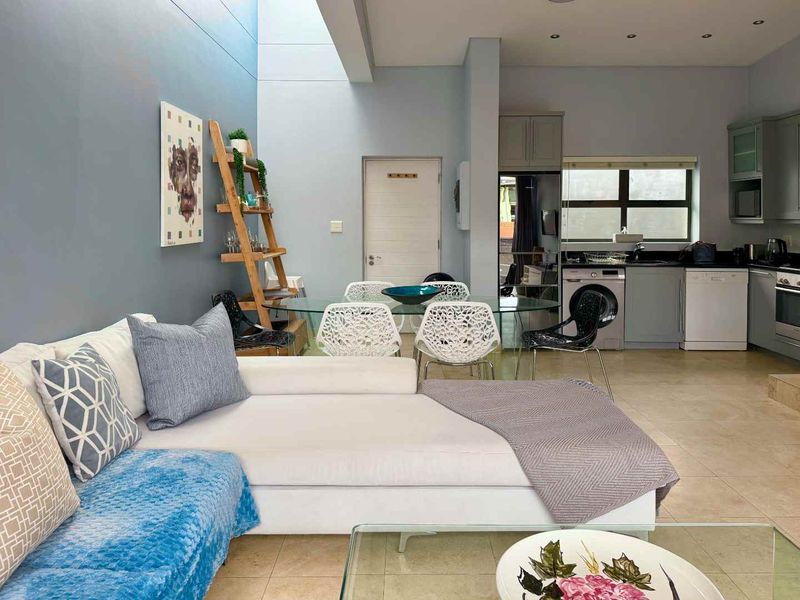 An open-plan living and kitchen area featuring tiled floors, a high ceiling with a skylight, and a functional kitchen with built-in cabinetry and appliances.