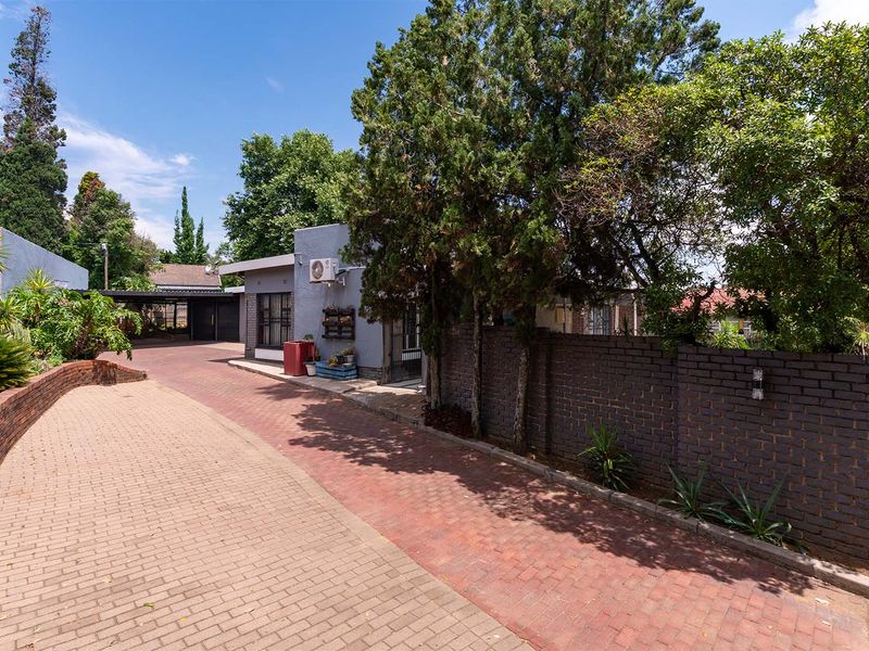 Front exterior view of the property featuring a paved driveway, brick boundary wall, and established trees leading to the entrance and carport area.