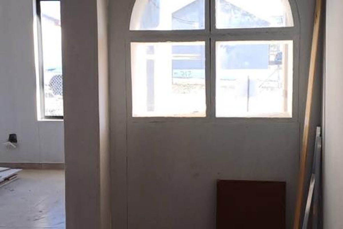 An unfinished interior space featuring tiled flooring and a distinctive arched window, currently undergoing renovation with exposed electrical fixtures.