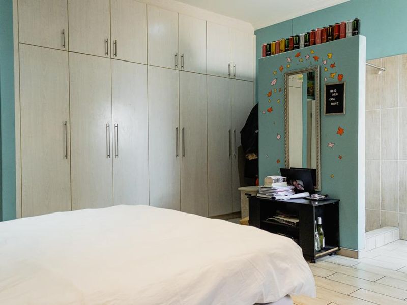 A bedroom featuring extensive built-in cabinetry, a partial partition wall, and an open-plan en-suite shower area with tiled flooring.