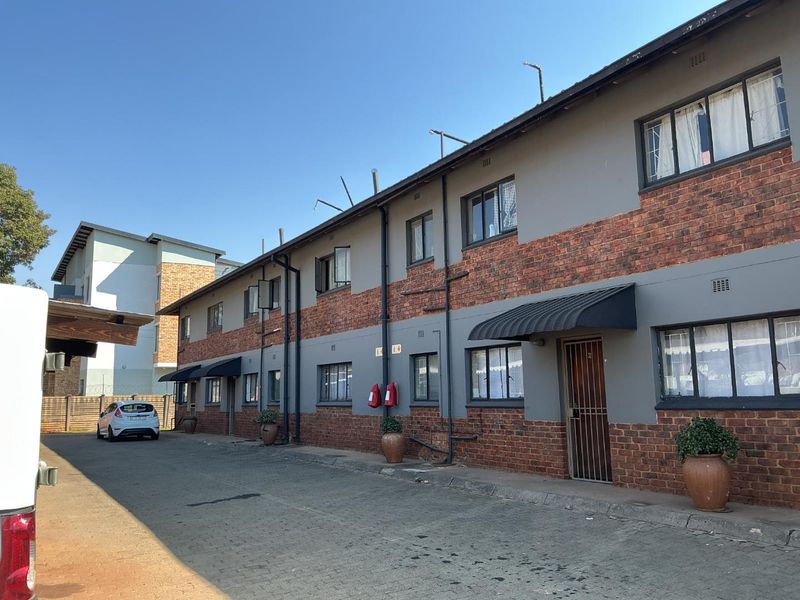 Exterior view of a multi-story apartment complex featuring a brick and painted facade, paved driveway, and security-fitted entrances.