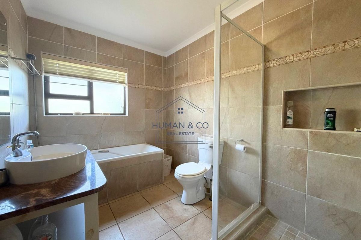 A functional bathroom featuring a glass-enclosed shower, a built-in bathtub, a vanity with a vessel sink, and neutral wall and floor tiling.
