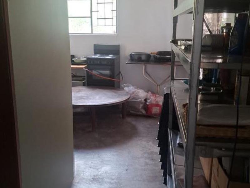 A functional scullery or utility area featuring concrete flooring, metal shelving, and a freestanding stove, requiring cosmetic updates to improve the space.