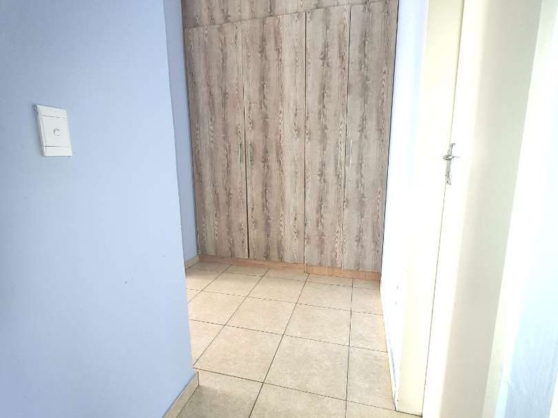A clean hallway featuring neutral tiled flooring and floor-to-ceiling built-in wooden cupboards, providing ample storage space.