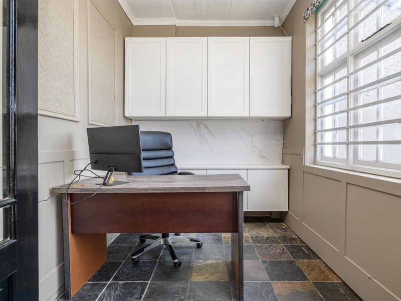 A functional home office featuring built-in white cabinetry, marble-look splashback, slate tile flooring, and wainscoting detail.