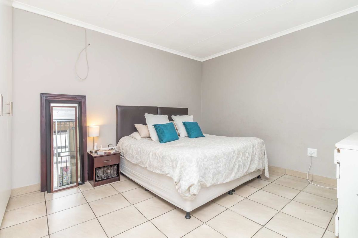 A spacious bedroom featuring neutral tiled flooring, built-in cupboard space, and a simple layout with direct access to a small balcony area.