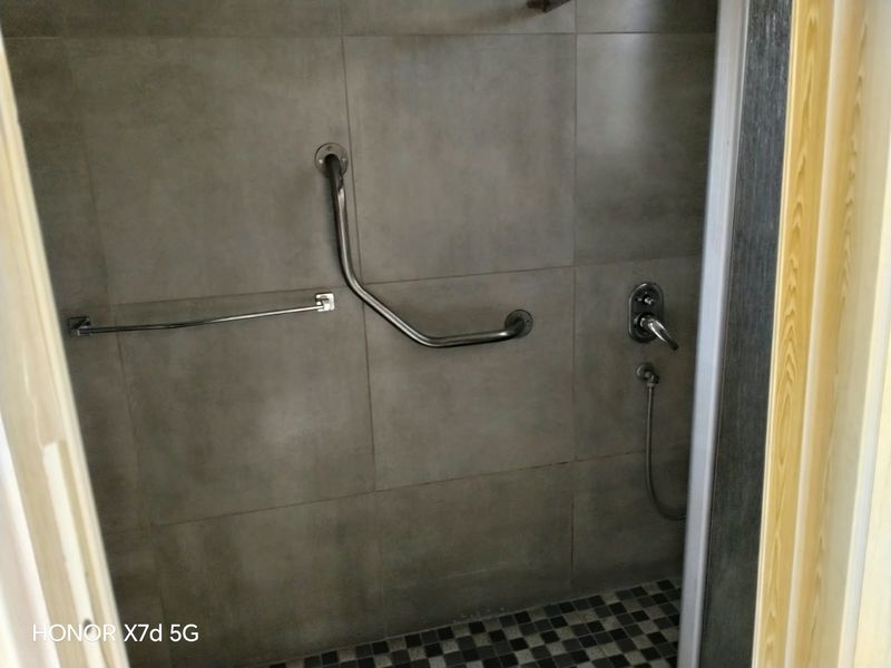 A functional shower enclosure featuring grey wall tiles, mosaic floor tiling, a chrome shower mixer, and a safety grab rail.
