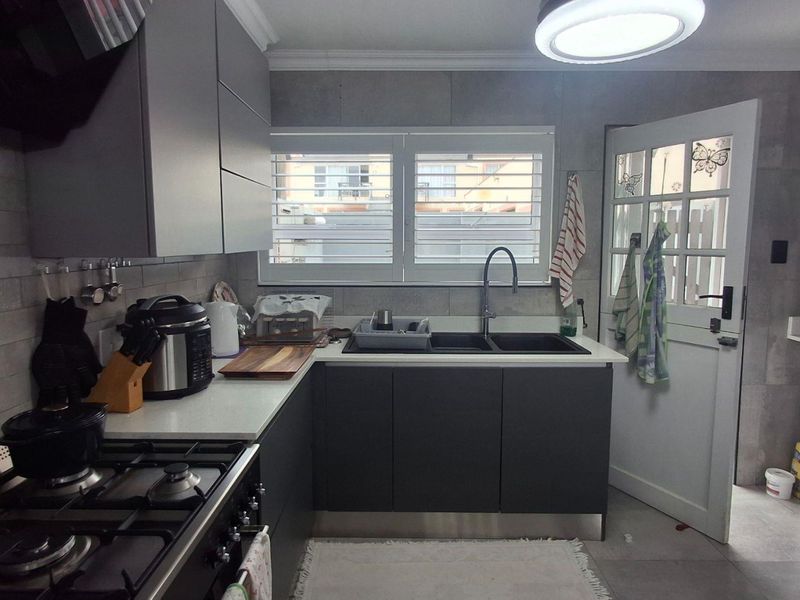 Modern kitchen featuring dark grey cabinetry, stone countertops, gas stove with extractor, double sink, and integrated laundry space with a side door exit.