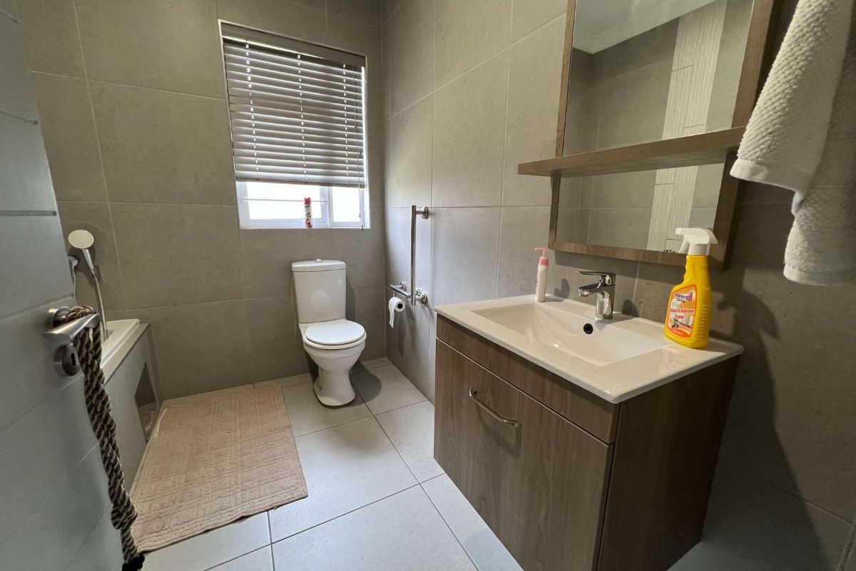 A modern bathroom featuring floor-to-ceiling grey tiling, a wall-mounted vanity with integrated basin, a toilet, and a shower-over-bath configuration with a grab rail.