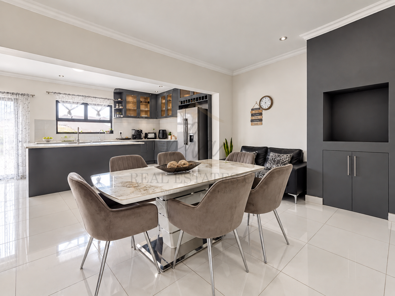 Modern open-plan dining and kitchen area featuring sleek dark cabinetry, a central island, polished tile flooring, and a built-in feature wall unit.