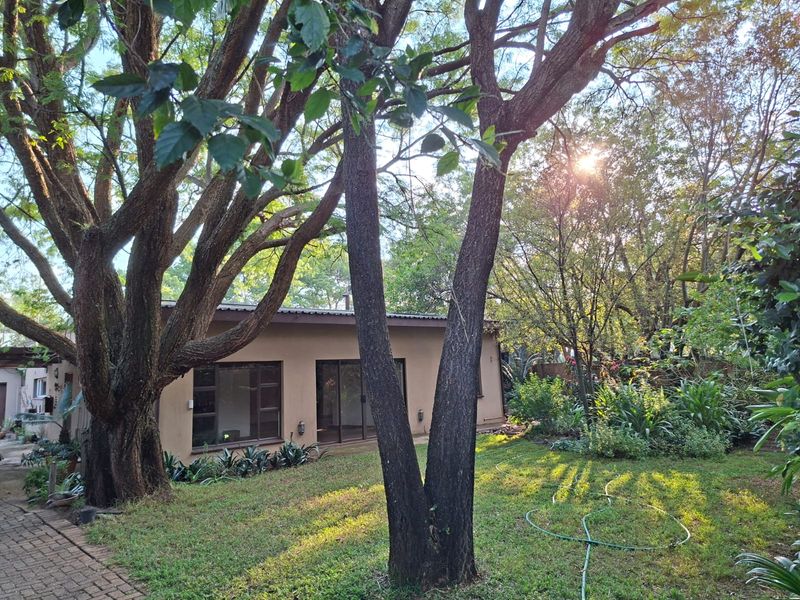 A view of the rear exterior of the house featuring a landscaped garden, mature trees, and sliding glass door access.
