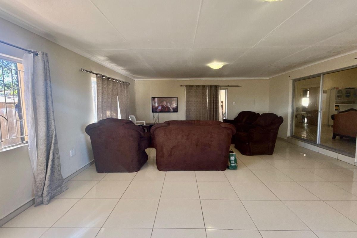 Spacious living area featuring neutral floor tiles, large windows for natural light, and sliding glass doors leading to an adjacent room.
