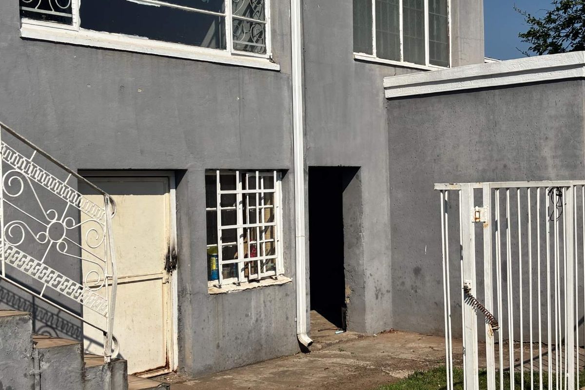 Rear exterior view of the property featuring a concrete paved area, external staircase, and security-fitted windows and doors.
