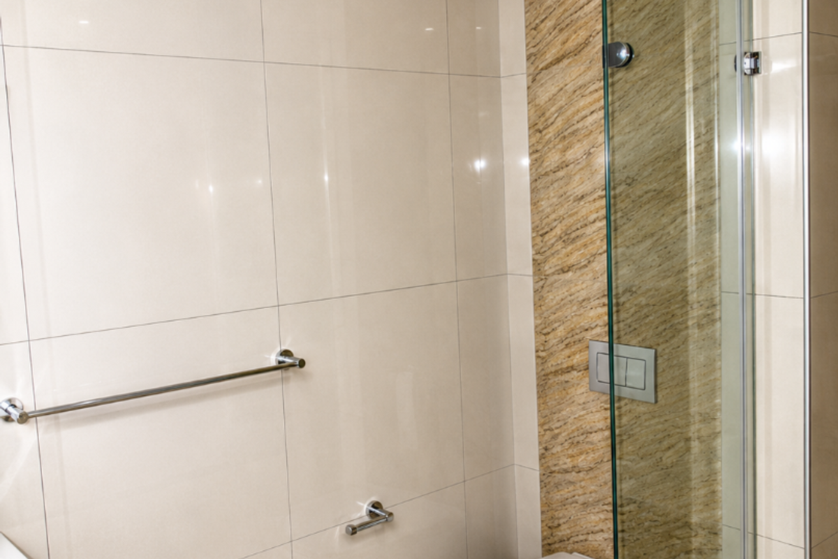 A modern bathroom featuring a wall-mounted toilet, glass shower screen, and neutral-toned wall and floor tiling with a decorative stone-look accent panel.