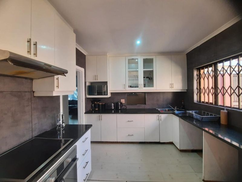 A functional kitchen featuring white cabinetry, dark granite countertops, built-in oven, extractor fan, and a window with a security gate.
