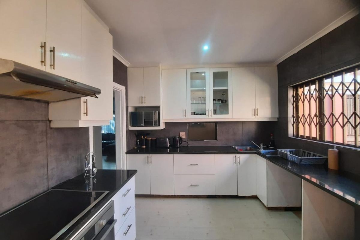 A functional kitchen featuring white cabinetry, dark granite countertops, built-in oven, extractor fan, and a window with a security gate.