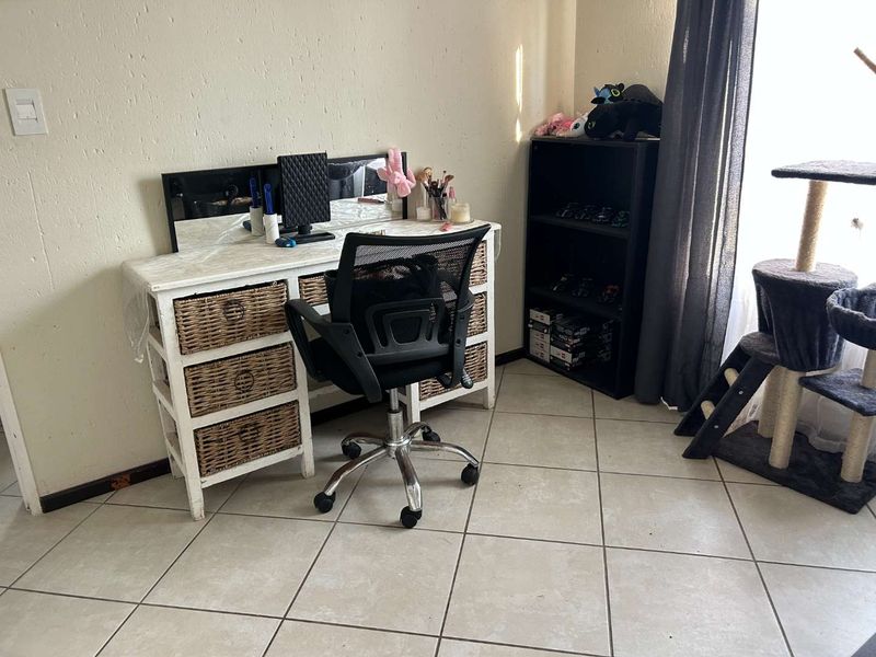 A bedroom space featuring neutral tiled flooring and a window with curtain rails, providing a functional area for a home office or study setup.