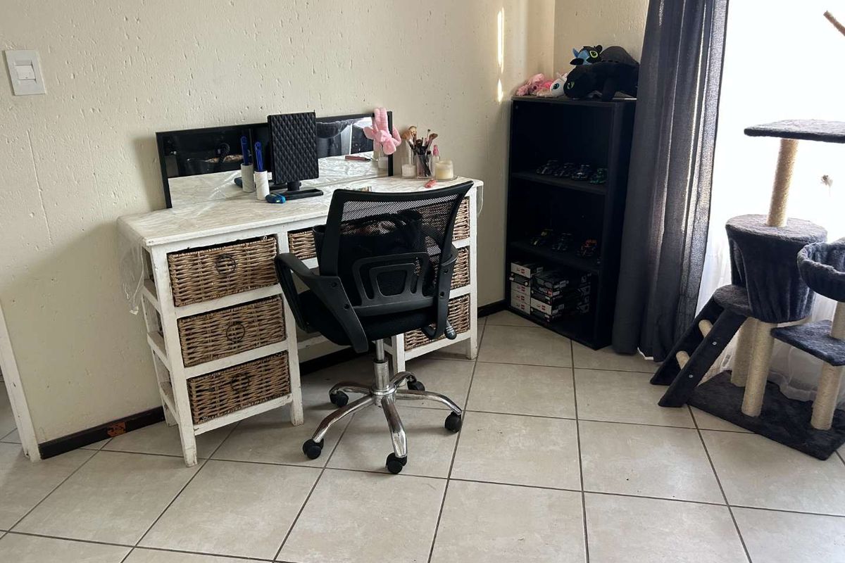 A bedroom space featuring neutral tiled flooring and a window with curtain rails, providing a functional area for a home office or study setup.