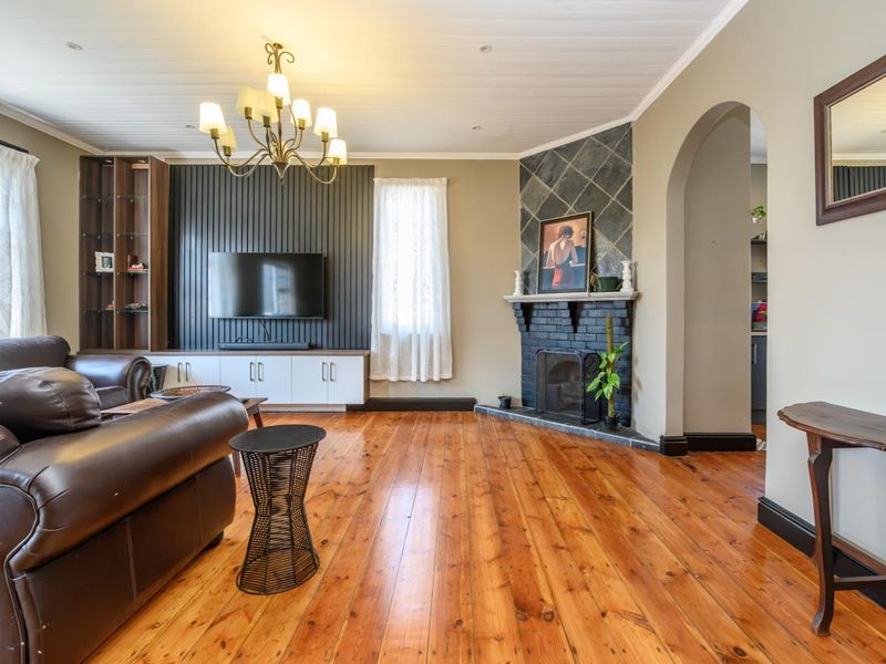 Spacious living room featuring polished hardwood floors, a feature fireplace with stone surround, built-in cabinetry, and an elegant arched entryway.