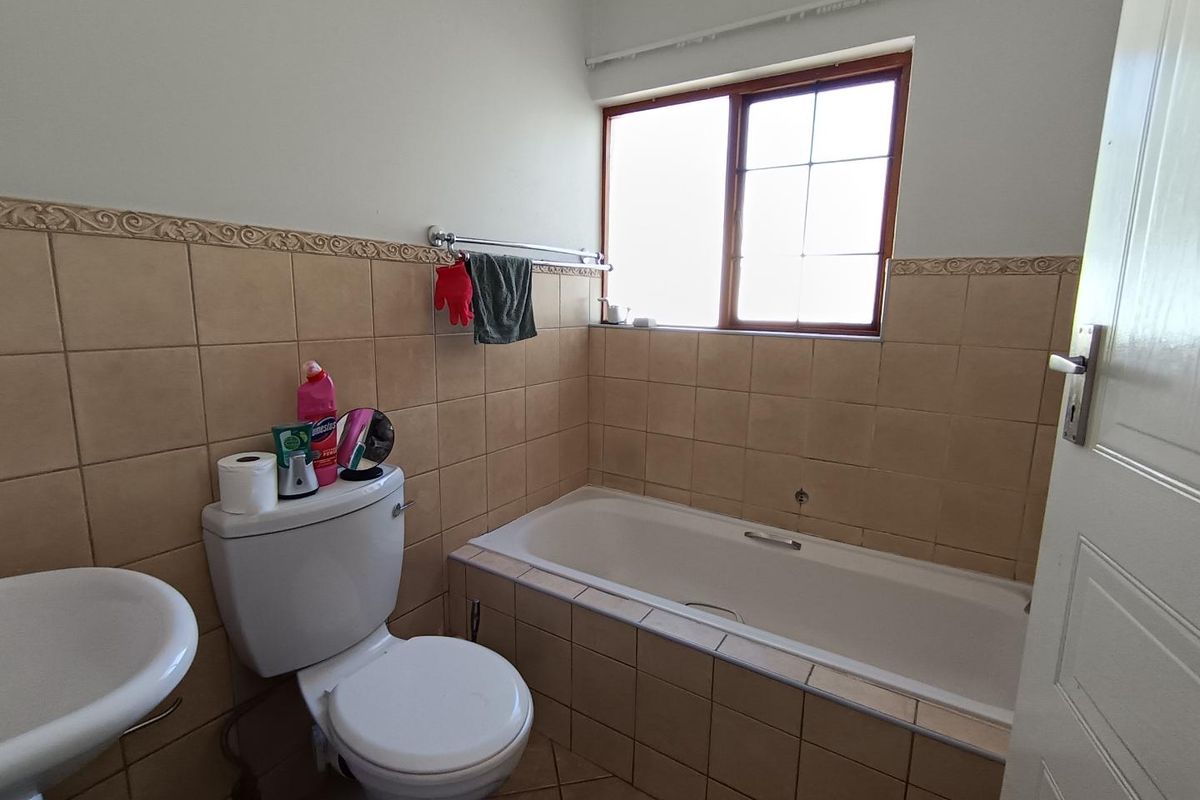 A functional bathroom featuring a built-in bathtub with tiled surround, a standard toilet, and a pedestal basin with neutral wall tiling.