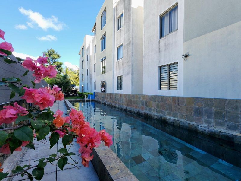 A lap pool area adjacent to a multi-story apartment building, featuring stone-clad pool edges and paved surrounds.