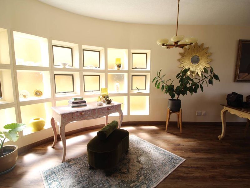 A living area featuring a curved wall with built-in illuminated display shelving and wood-look laminate flooring.