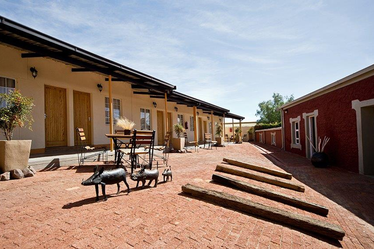 A paved courtyard area featuring a row of hotel room entrances with covered walkways and a rustic red brick building facade.