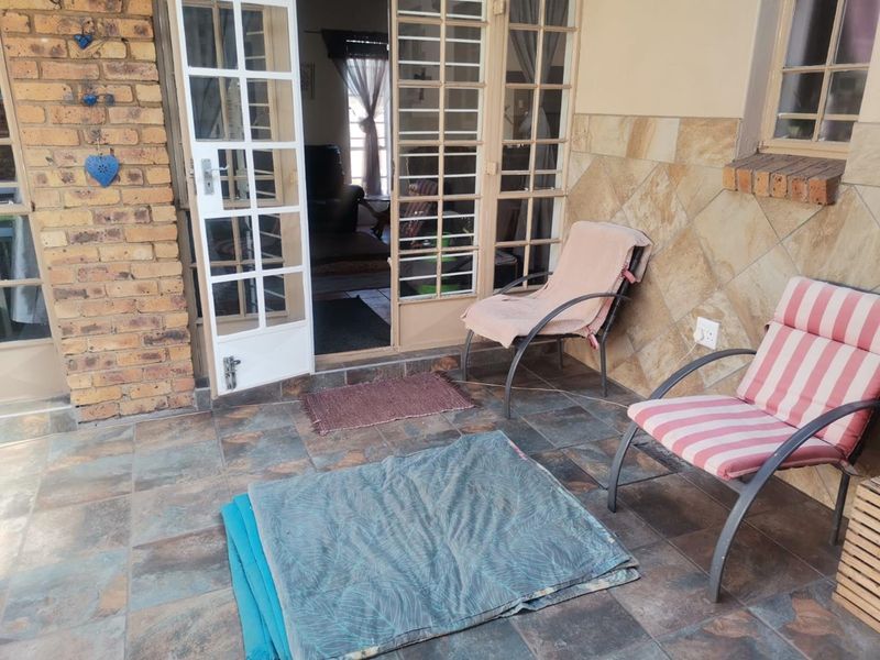 A covered patio area featuring tiled flooring, stone wall cladding, and access to the interior through white-framed french doors.