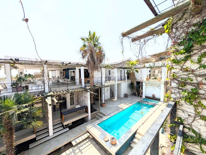A multi-level outdoor entertainment area featuring a swimming pool, tiered concrete decking, and timber pergolas with established climbing greenery.