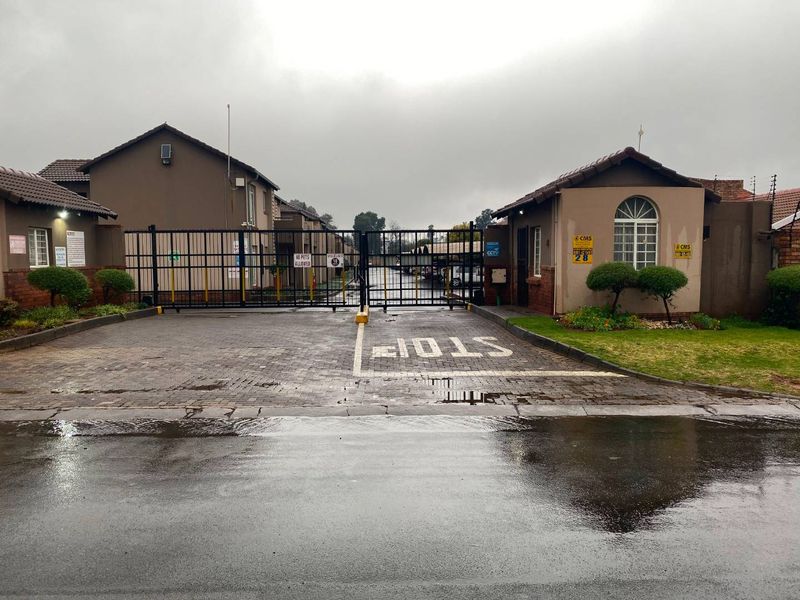 Front entrance view of an apartment complex featuring a secure gated access point, paved driveway, and well-maintained brick facade buildings.