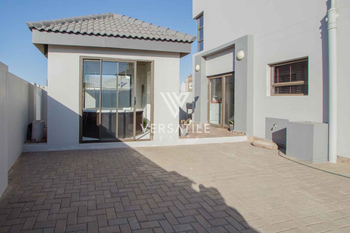 A paved rear courtyard area featuring a modern structure with sliding glass doors and tiled roofing, providing a clean and functional outdoor space.
