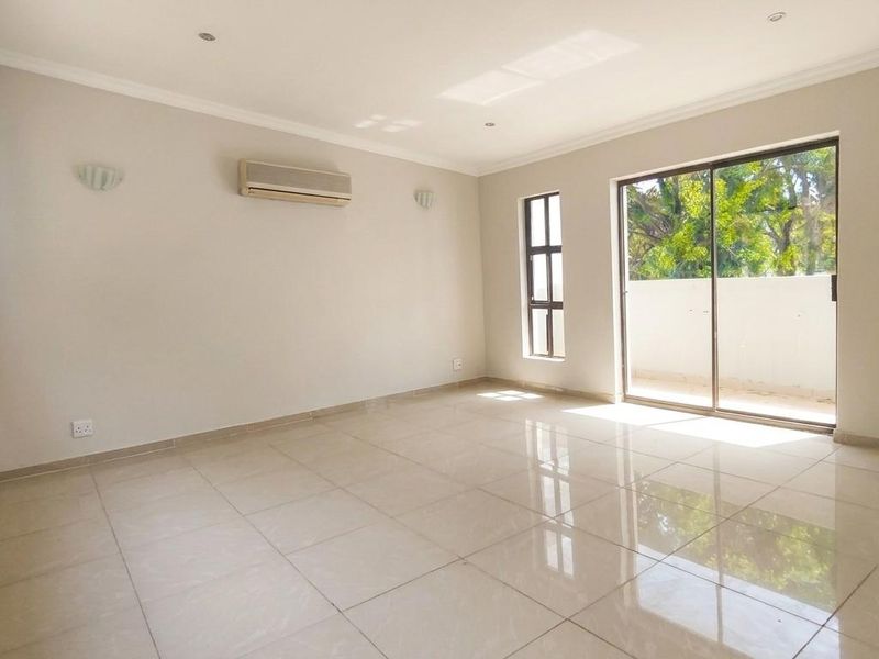A bright, spacious, and empty living room featuring polished tile flooring, a wall-mounted air conditioner, and large sliding glass doors leading to a balcony.