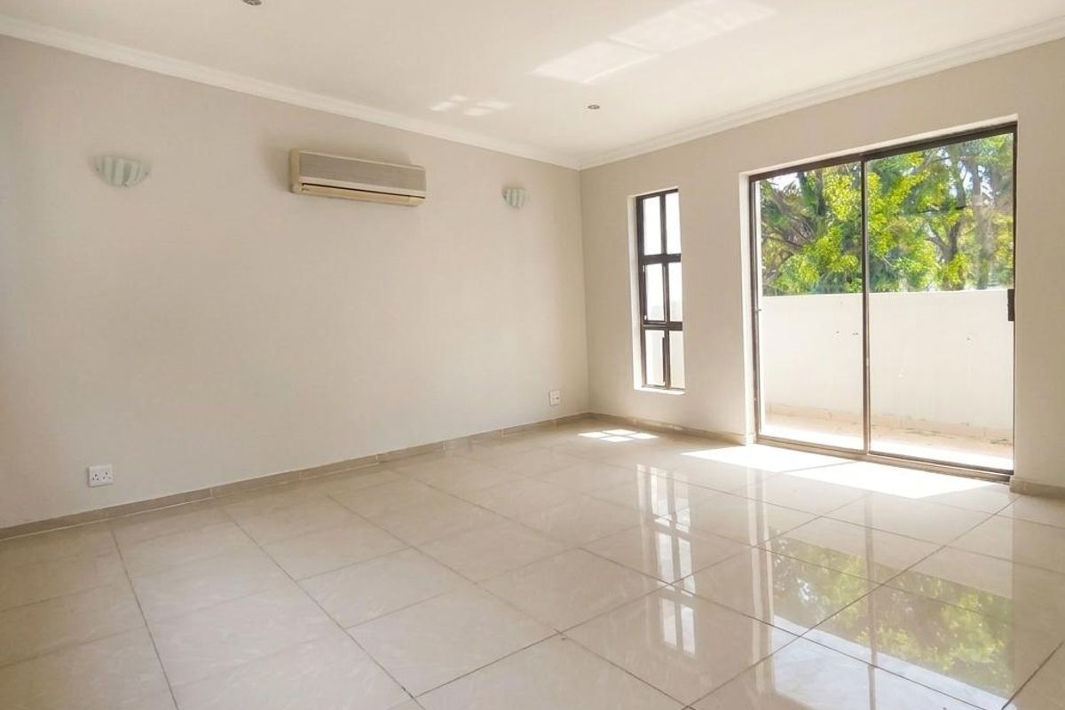 A bright, spacious, and empty living room featuring polished tile flooring, a wall-mounted air conditioner, and large sliding glass doors leading to a balcony.