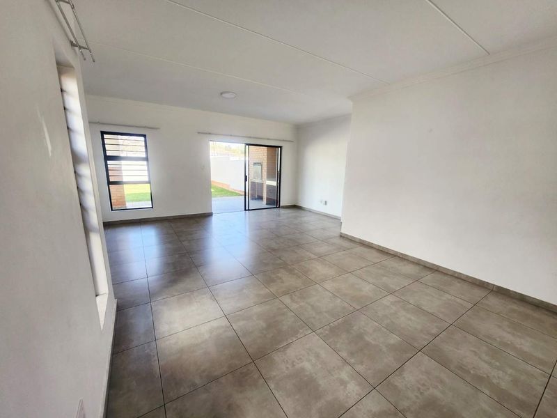 Spacious, open-plan living area featuring neutral tiled flooring, large windows, and a sliding glass door providing direct access to the rear garden.
