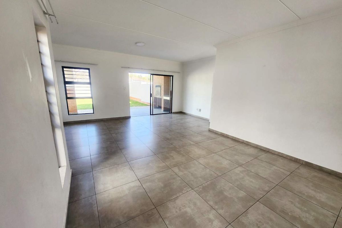 Spacious, open-plan living area featuring neutral tiled flooring, large windows, and a sliding glass door providing direct access to the rear garden.