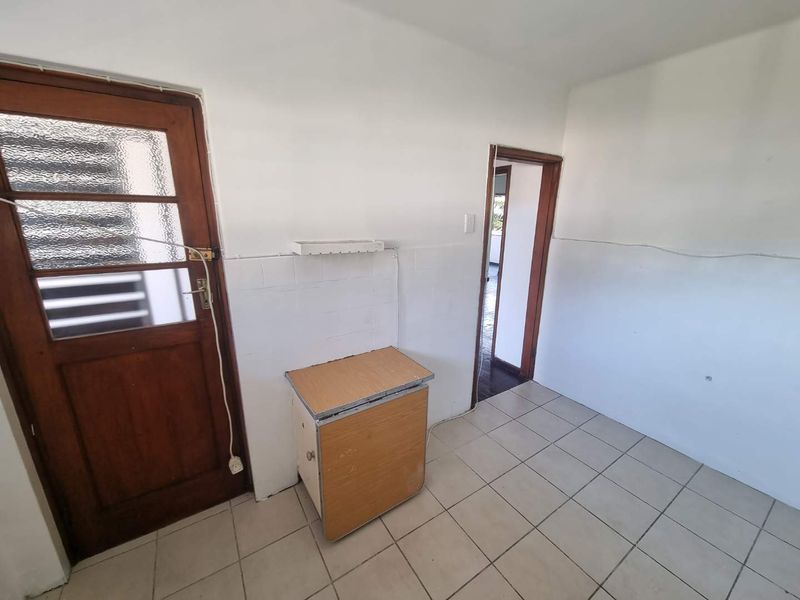 A basic, empty kitchen area featuring tiled flooring, tiled splashbacks, and a timber door, offering a blank canvas for renovation.