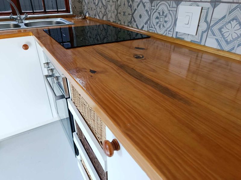A well-maintained kitchen featuring a polished wooden countertop, stainless steel sink, built-in oven, electric hob, and decorative patterned tile backsplash.