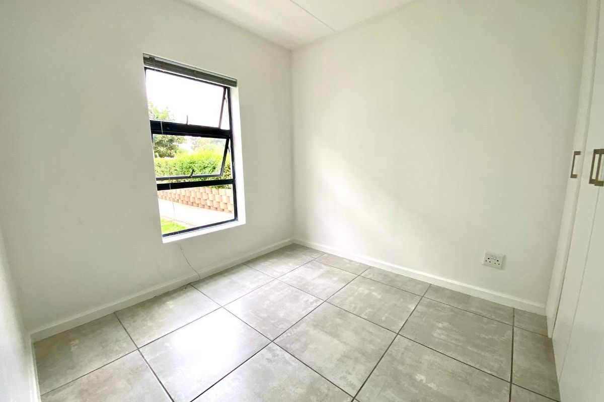 A bright, empty bedroom featuring neutral tiled flooring, built-in cupboards, and a window providing natural light.