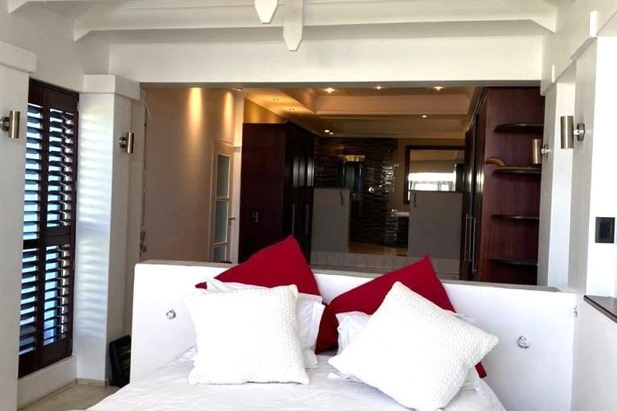 Spacious bedroom featuring a vaulted ceiling with exposed white beams, integrated wall lighting, and an open-plan layout leading to an en-suite bathroom area.
