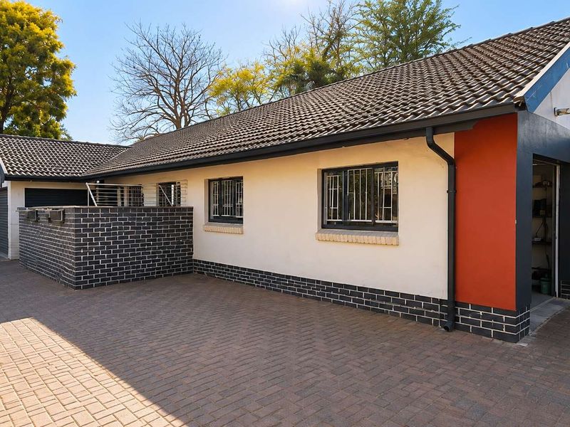 Front exterior view of the house featuring a paved driveway, brick accents, tiled roof, and secure window bars.