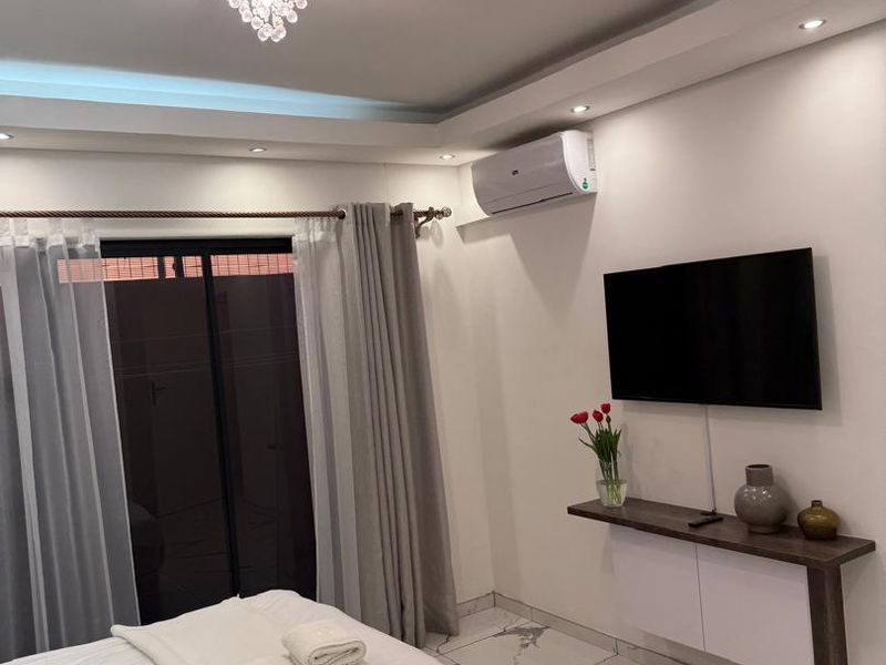 Modern bedroom featuring marble-look floor tiles, a floating wall-mounted cabinet, recessed ceiling lighting, and a crystal chandelier.