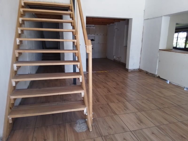 Open plan retail space featuring wood-look tiled flooring and a central wooden staircase, offering a blank canvas for custom interior design and layout.