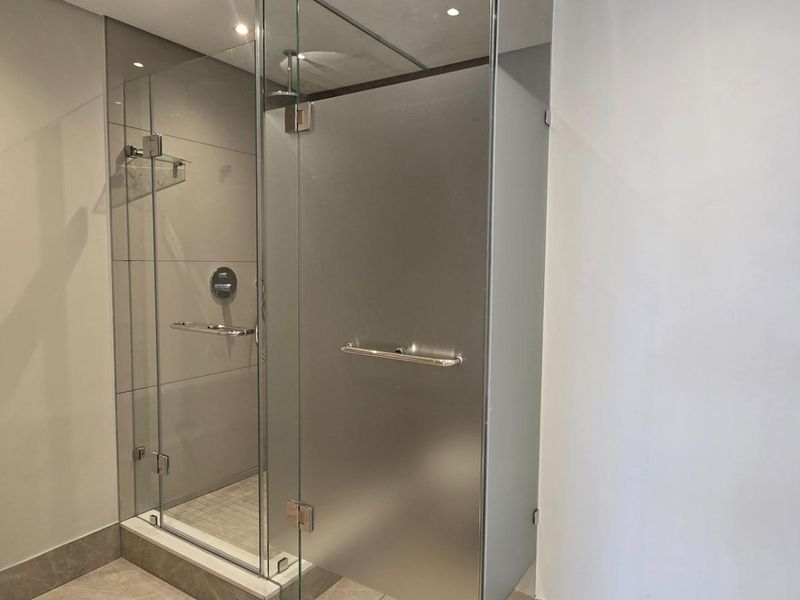 Modern bathroom featuring a sleek glass shower enclosure with a frosted door, contemporary wall-mounted fixtures, and neutral tiling throughout.