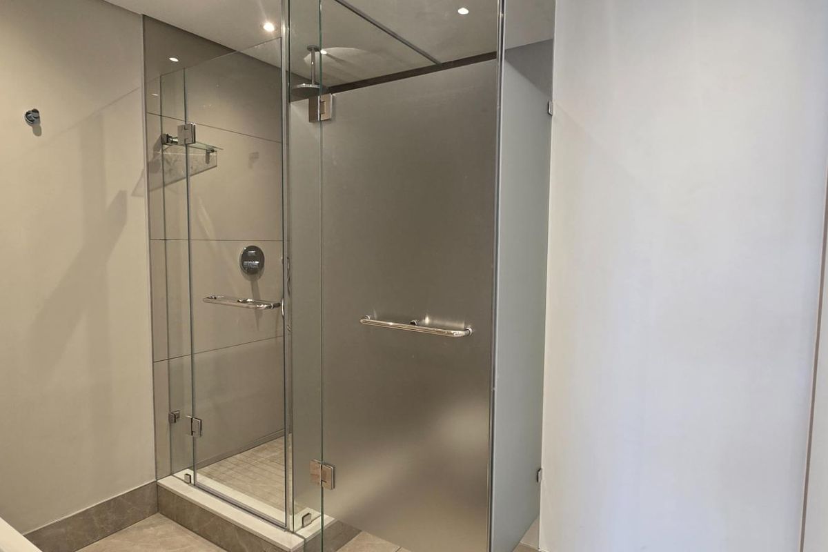 Modern bathroom featuring a sleek glass shower enclosure with a frosted door, contemporary wall-mounted fixtures, and neutral tiling throughout.