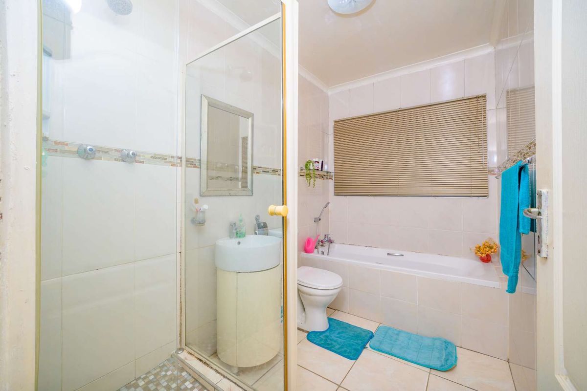 A functional bathroom featuring a separate shower enclosure, bathtub, pedestal basin, and toilet with neutral wall and floor tiling.